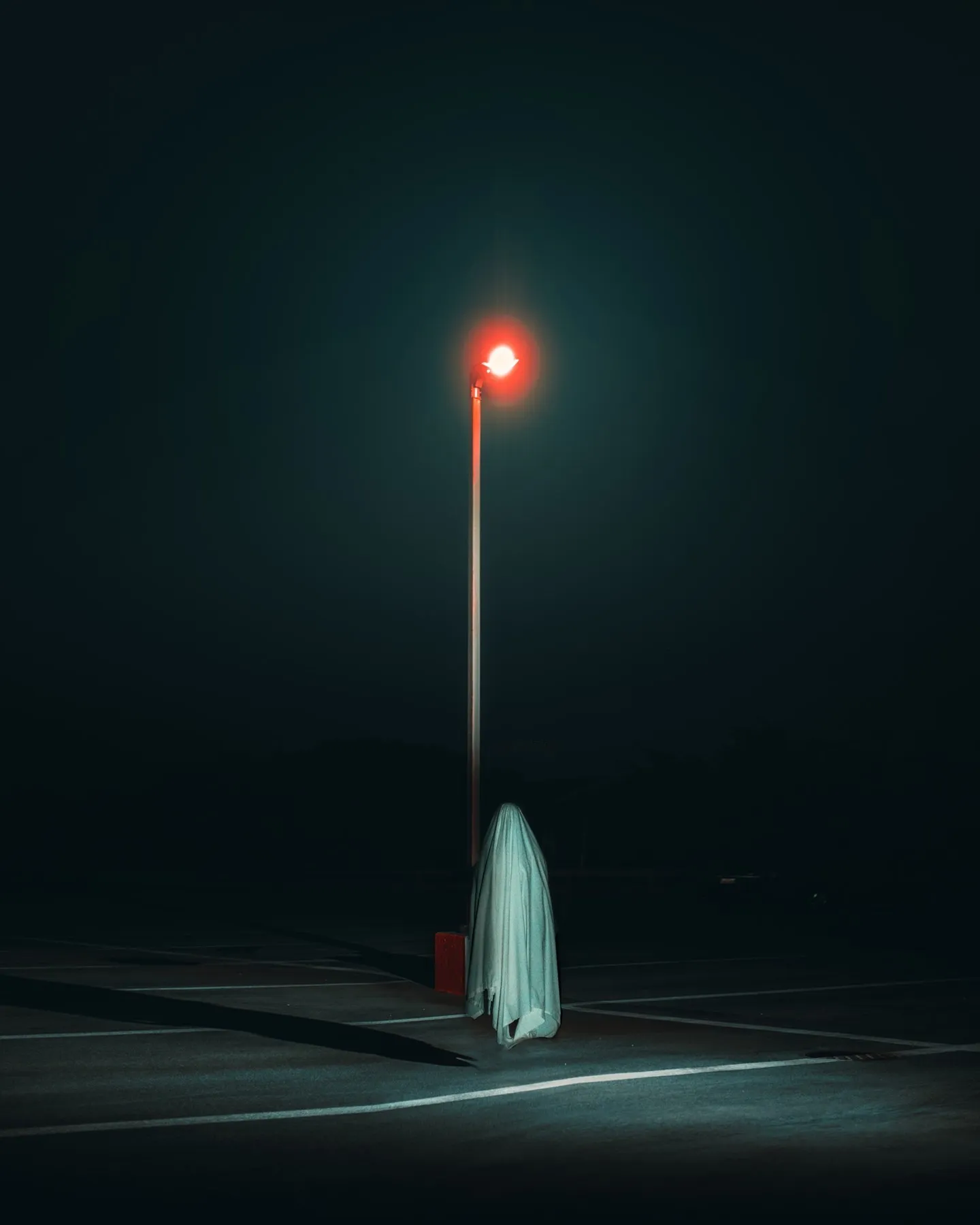 A street lamp with a red bulb on a foggy night, a draped white cloth figure standing beneath it.