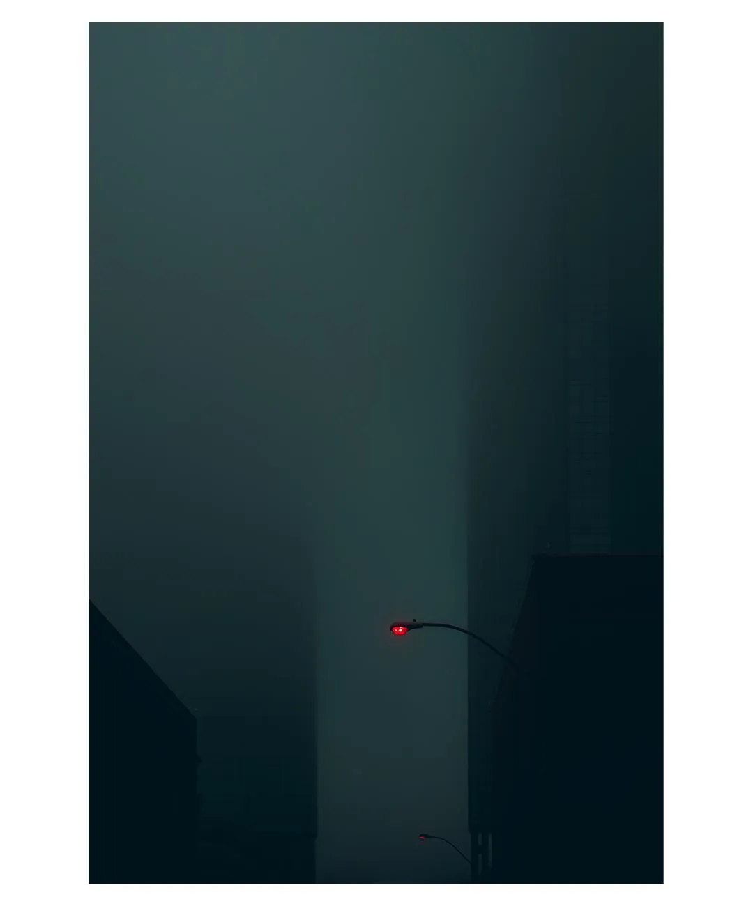A minimal dark building corner in haze, a single small red light.
