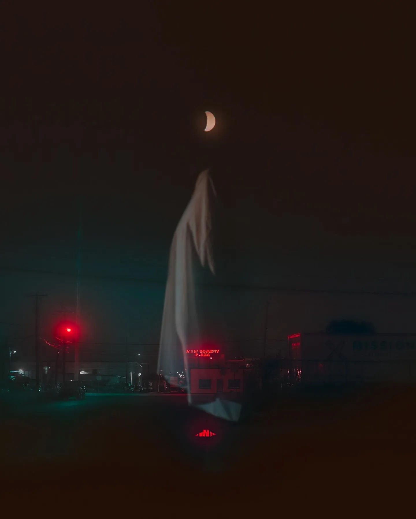 A white cloth figure raised on a pole at night, red lights and a parked car below.