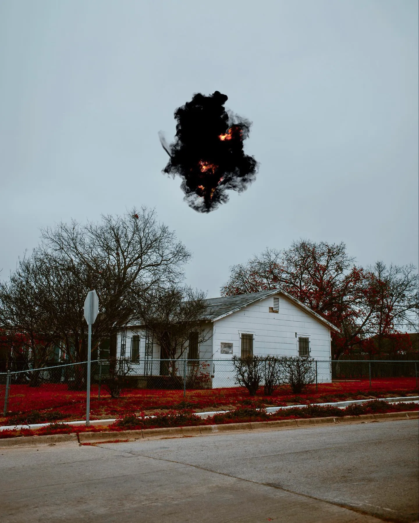 A house on a residential street with a dark mass suspended above it against a pale grey sky.