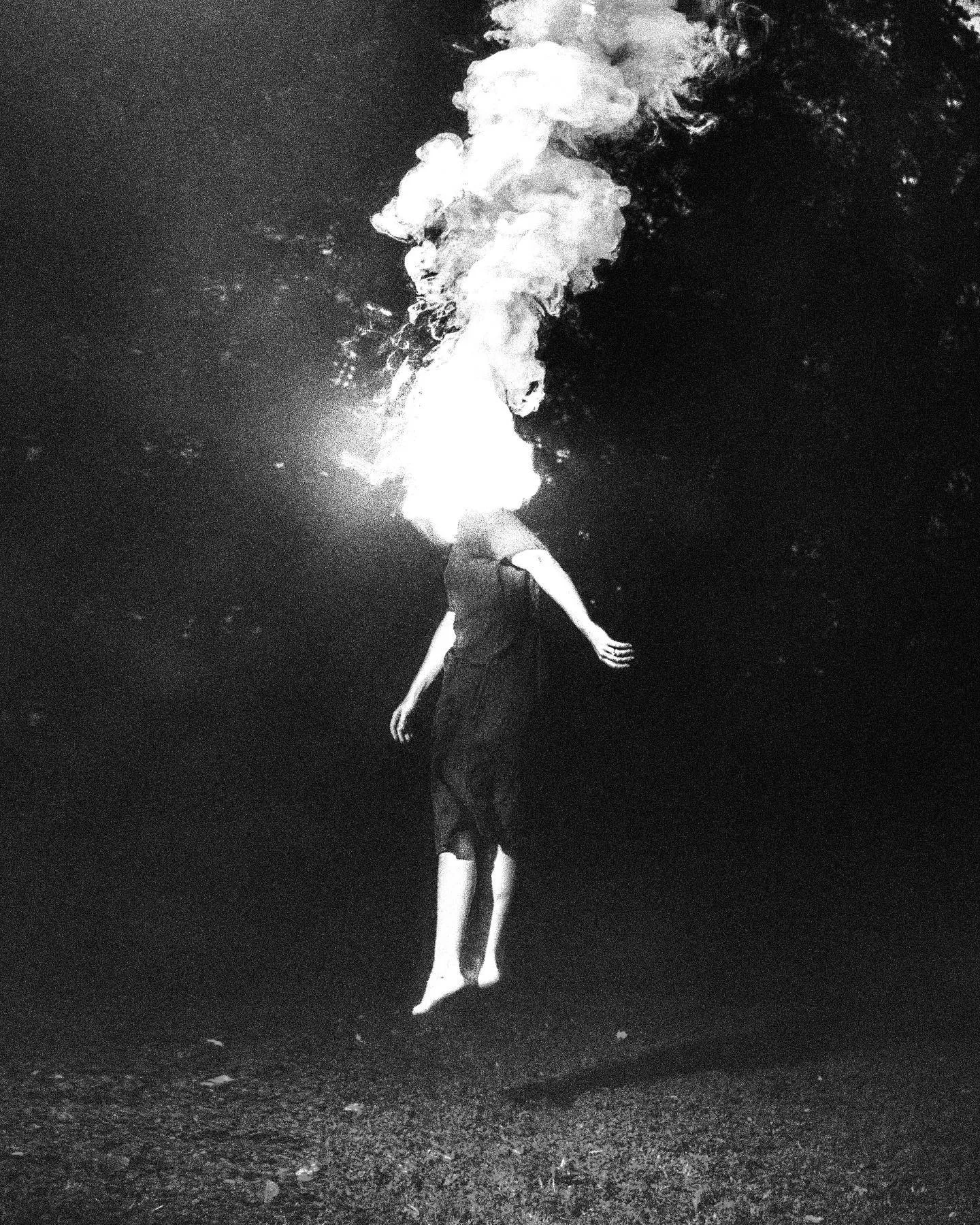 Black and white: a figure with arms out and a bright burst of white smoke above the head.