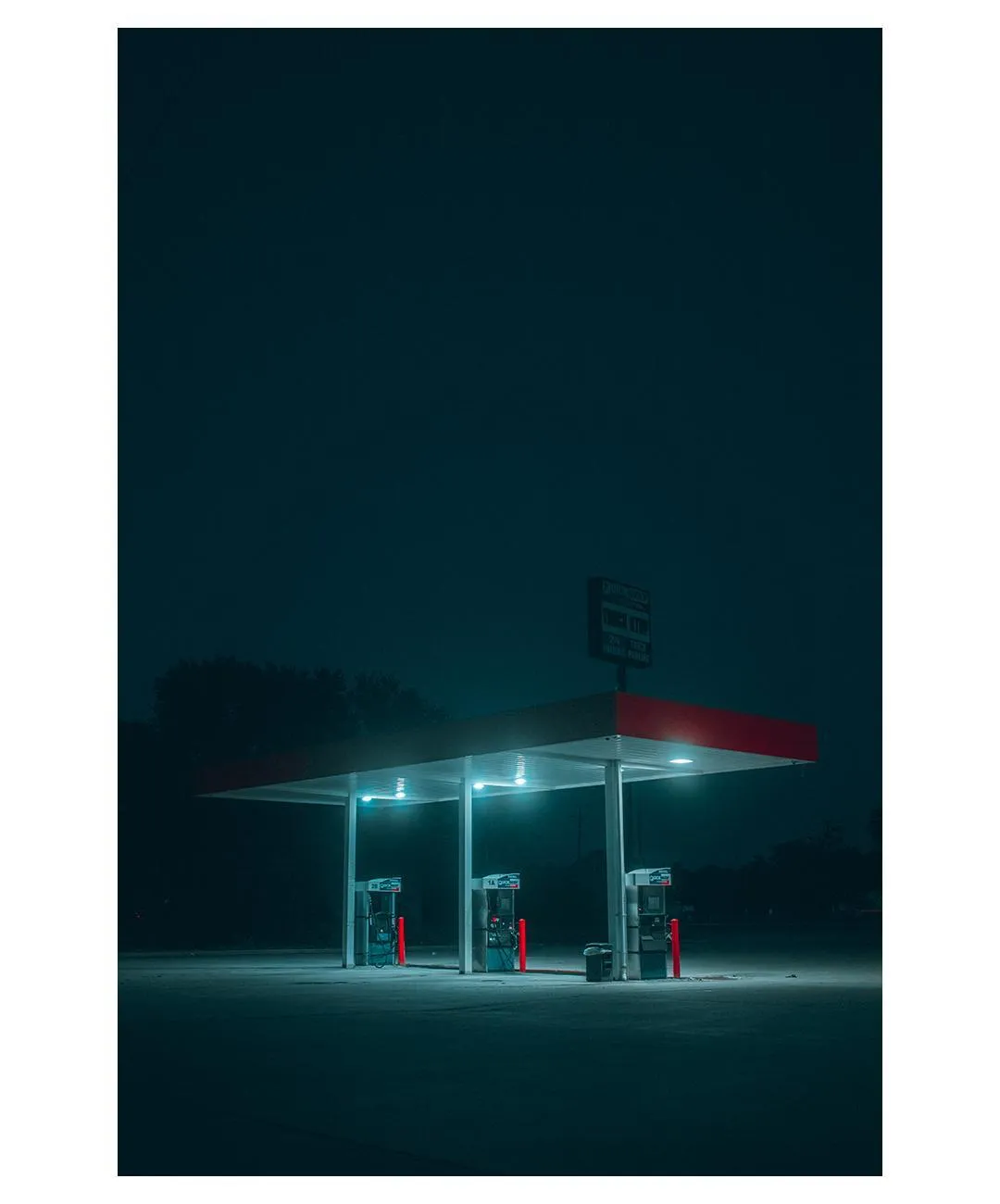 A gas station at night lit with teal and red light.